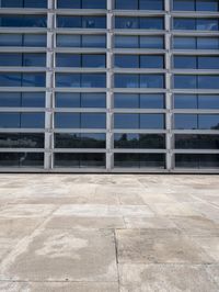 a cement floor in front of an industrial glass building with some windows behind it in a flat light