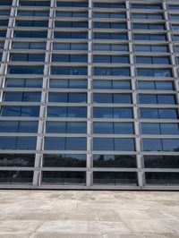 a cement floor in front of an industrial glass building with some windows behind it in a flat light