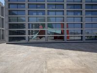 a cement floor in front of an industrial glass building with some windows behind it in a flat light