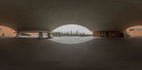 view of a circular concrete building from inside out with trees in the distance through the oval doorway