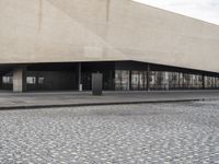 a building with glass windows and a stone floor by the sidewalk and people on a street