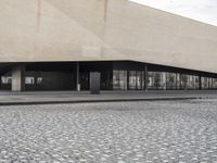 a building with glass windows and a stone floor by the sidewalk and people on a street