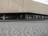 a building with glass windows and a stone floor by the sidewalk and people on a street