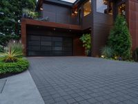 a modern home designed with a paved driveway, trees and bushes surrounding the front door