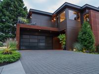 a modern home designed with a paved driveway, trees and bushes surrounding the front door