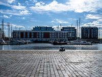 a small brick walkway next to a body of water with boats on it and buildings in the background