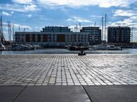 a small brick walkway next to a body of water with boats on it and buildings in the background