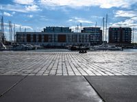 a small brick walkway next to a body of water with boats on it and buildings in the background