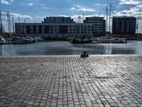 a small brick walkway next to a body of water with boats on it and buildings in the background