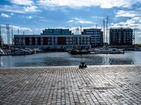 a small brick walkway next to a body of water with boats on it and buildings in the background