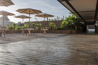 an empty patio area with tables and umbrellas above it and sunbeams over the courtyard