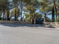 the driveway of the villa is quiet on this sunny day that it is very shaded with trees and stone,