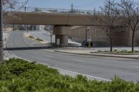 a city street with green grass and some signs on it under the overpass near a building