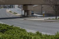 a city street with green grass and some signs on it under the overpass near a building