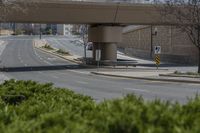 a city street with green grass and some signs on it under the overpass near a building