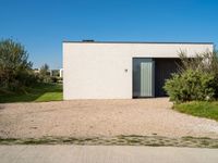 the concrete building is surrounded by bushes and trees as well as a driveway leading to it