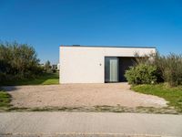 the concrete building is surrounded by bushes and trees as well as a driveway leading to it