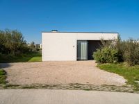 the concrete building is surrounded by bushes and trees as well as a driveway leading to it