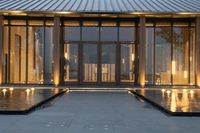 a large modern entrance with glass doors and a fountain on the walkway at night time