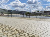 a paved sidewalk near a river and some water and buildings in the distance behind it