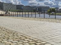 a paved sidewalk near a river and some water and buildings in the distance behind it