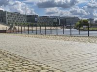 a paved sidewalk near a river and some water and buildings in the distance behind it