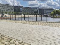 a paved sidewalk near a river and some water and buildings in the distance behind it