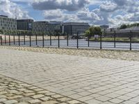 a paved sidewalk near a river and some water and buildings in the distance behind it