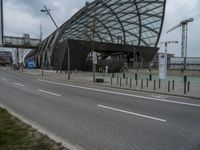 an open, curved building sitting next to a river with lots of traffic passing by