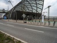 an open, curved building sitting next to a river with lots of traffic passing by