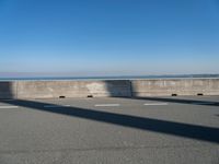 a bridge over the ocean with construction equipment in the background and two people walking on it