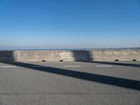 a bridge over the ocean with construction equipment in the background and two people walking on it