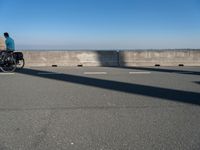 a bridge over the ocean with construction equipment in the background and two people walking on it