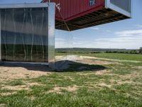 a metal building is connected to an open green field and a red one with its roof attached