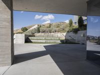 an outdoor courtyard with concrete walls and a bench with a red bag in it and the stairs up and mountains behind