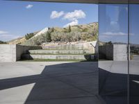 an outdoor courtyard with concrete walls and a bench with a red bag in it and the stairs up and mountains behind