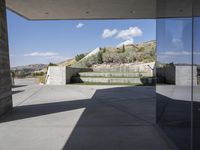 an outdoor courtyard with concrete walls and a bench with a red bag in it and the stairs up and mountains behind