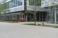 a glass building with tables and chairs and a bench in the park area next to it