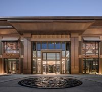 the building is brown and has many windows and lights around it the entrance is a circle that is in the middle of the courtyard