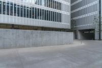 a large, modern building with the corner covered in concrete near a parking lot with trees and sidewalk