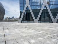 the square concrete tiles outside of the building in front of the sky are reflecting through the glass windows
