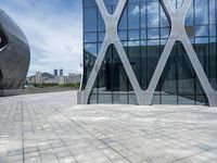 the square concrete tiles outside of the building in front of the sky are reflecting through the glass windows