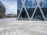 the square concrete tiles outside of the building in front of the sky are reflecting through the glass windows