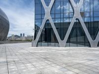 the square concrete tiles outside of the building in front of the sky are reflecting through the glass windows