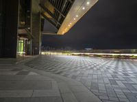 there is a walkway that extends out into an open air zone at night time, with buildings visible behind