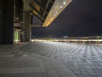 there is a walkway that extends out into an open air zone at night time, with buildings visible behind