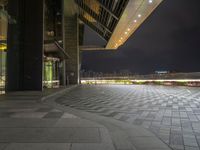 there is a walkway that extends out into an open air zone at night time, with buildings visible behind