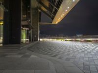 there is a walkway that extends out into an open air zone at night time, with buildings visible behind