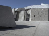 a concrete block with metal strips on it in front of an art museum structure with another building on the other side