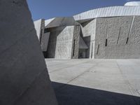 a concrete block with metal strips on it in front of an art museum structure with another building on the other side